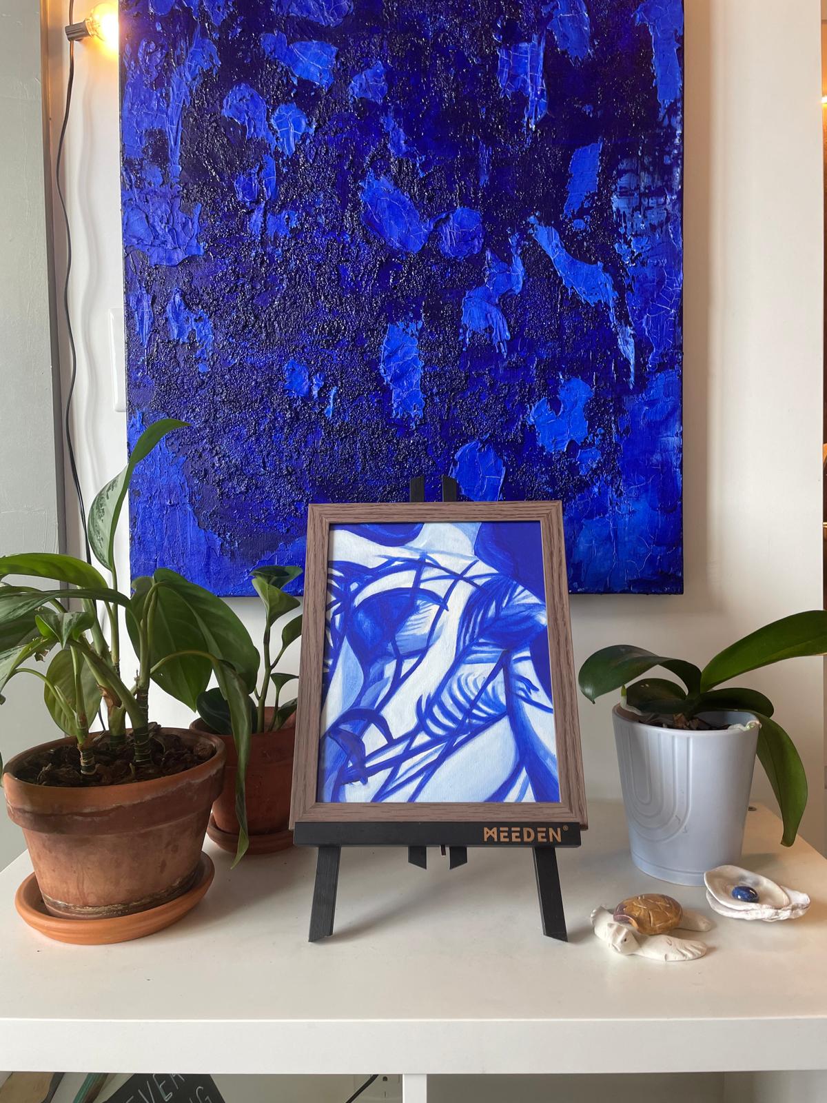 Large textured cobalt painting above a small framed piece and plants