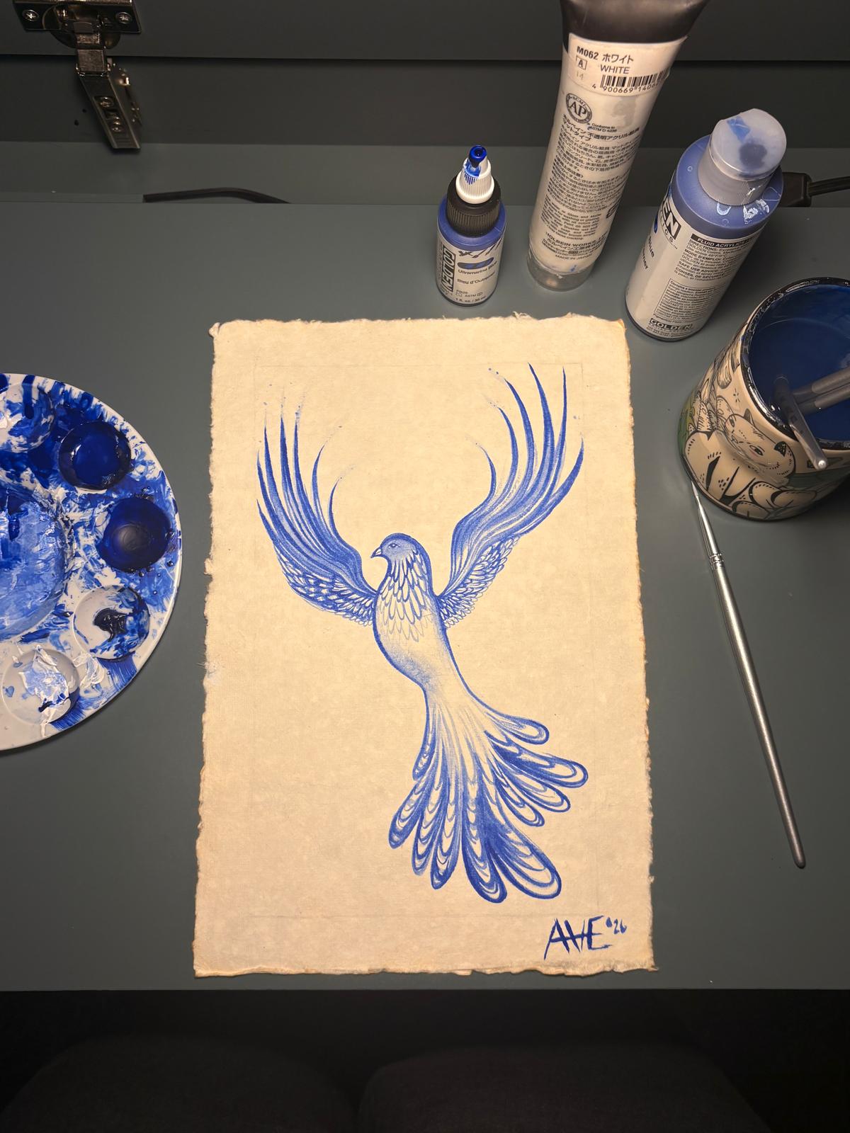 Blue phoenix on handmade paper beside paints