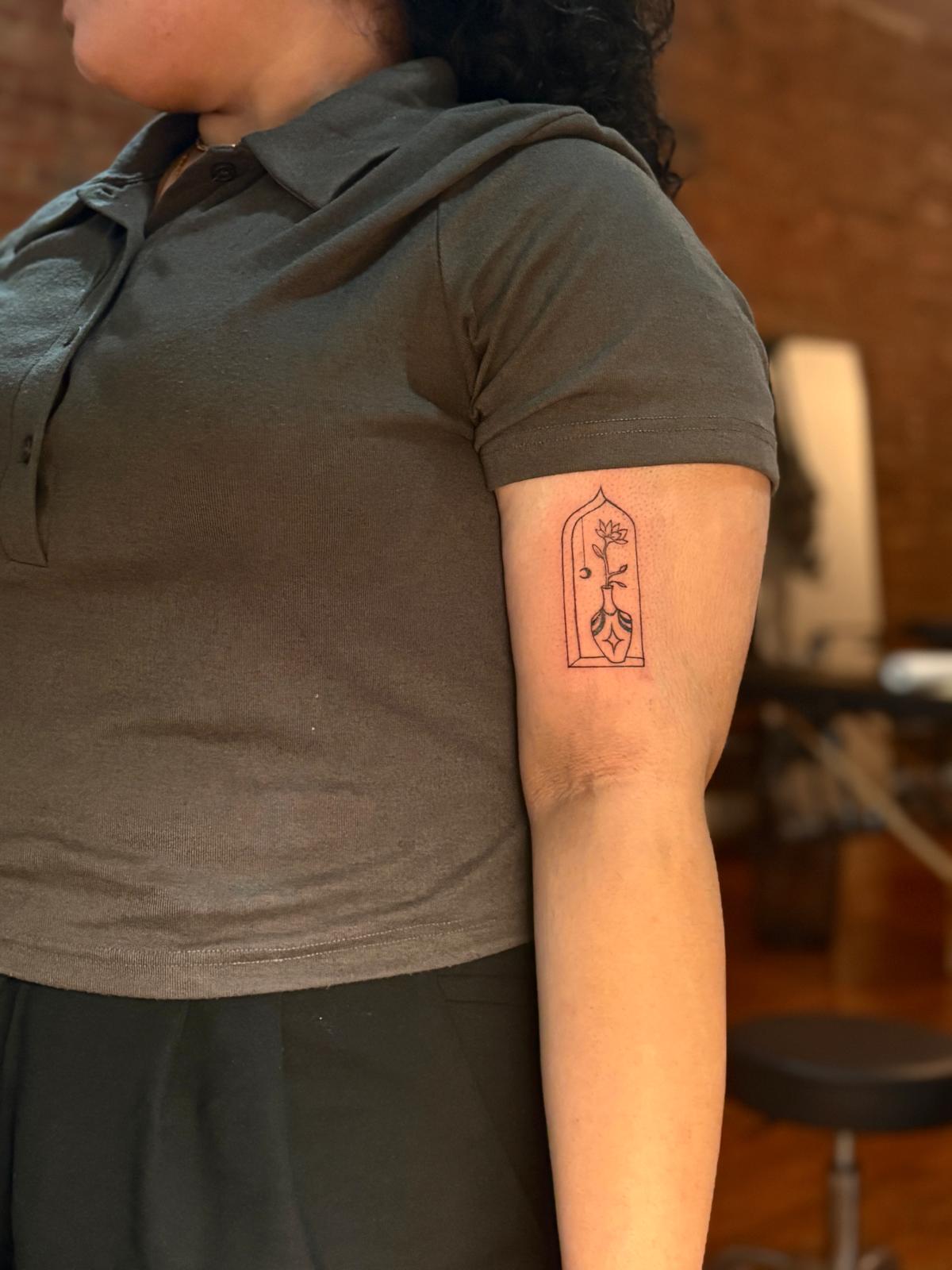 Small arched flower tattoo on an upper arm