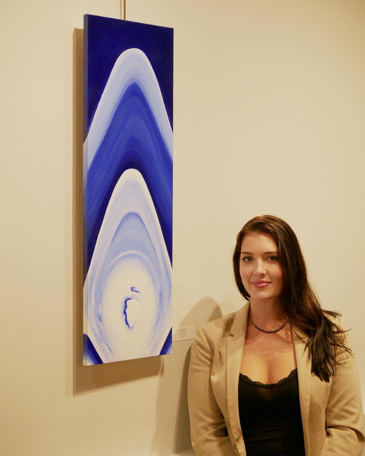 Ash Van Eyk beside a blue painting in a gallery