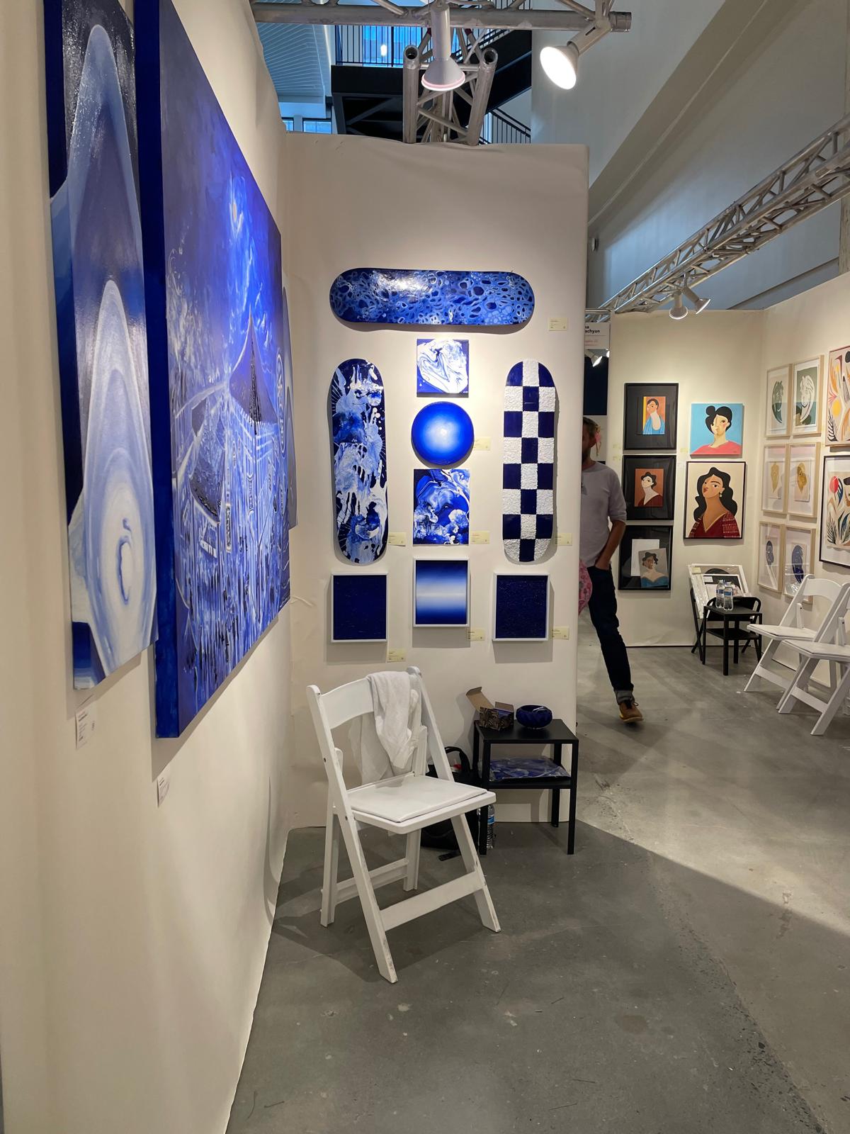 Art fair booth hung with blue paintings and painted skateboards