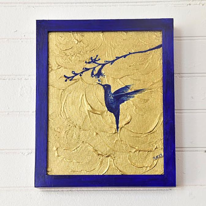Blue hummingbird on a branch over textured gold, in a cobalt frame