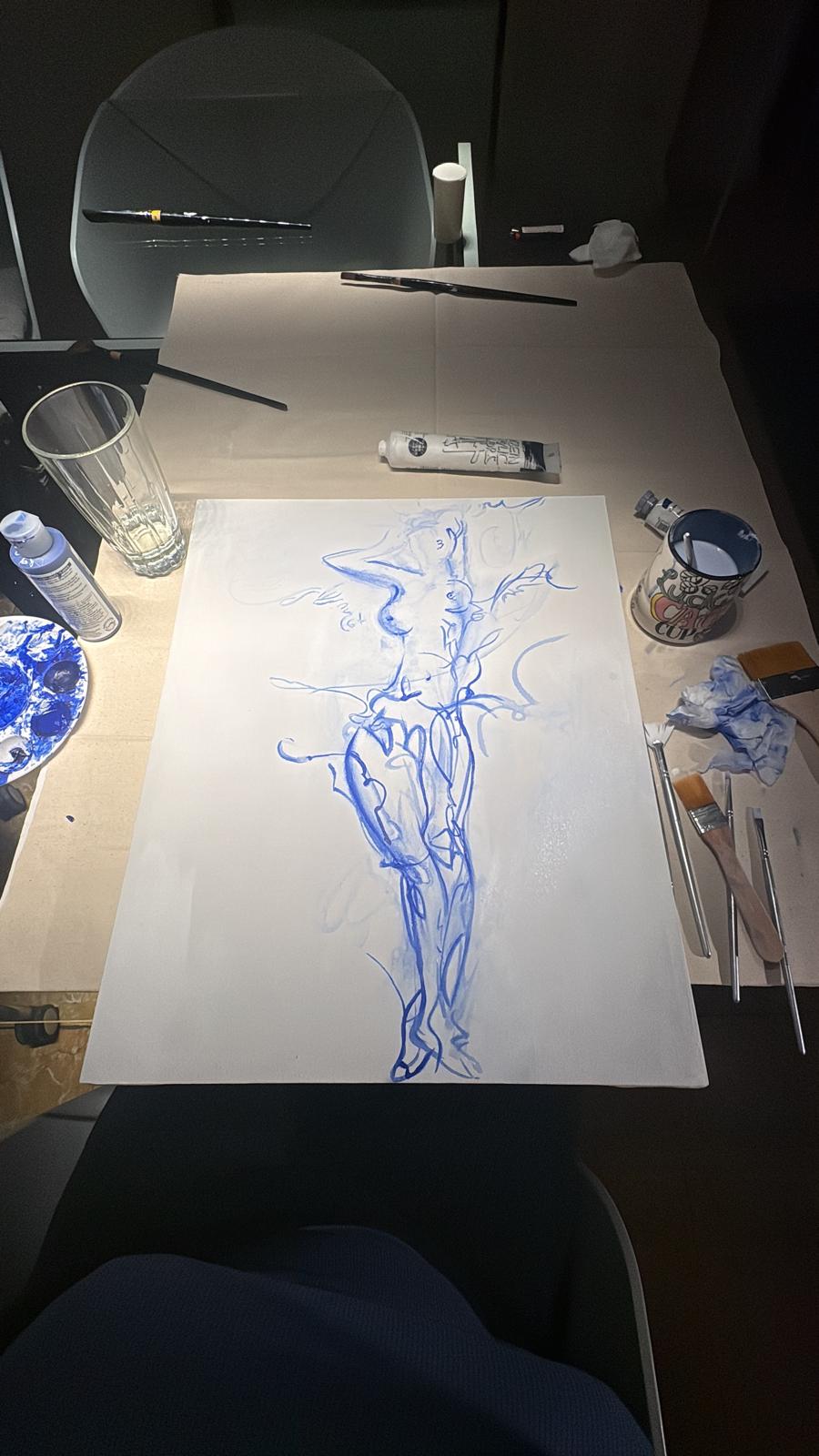 Blue figure painting in progress on a worktable with brushes and paint