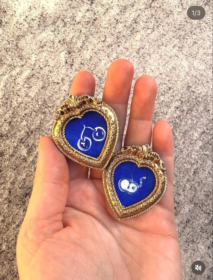 Two tiny gold heart frames with blue paintings held in a palm