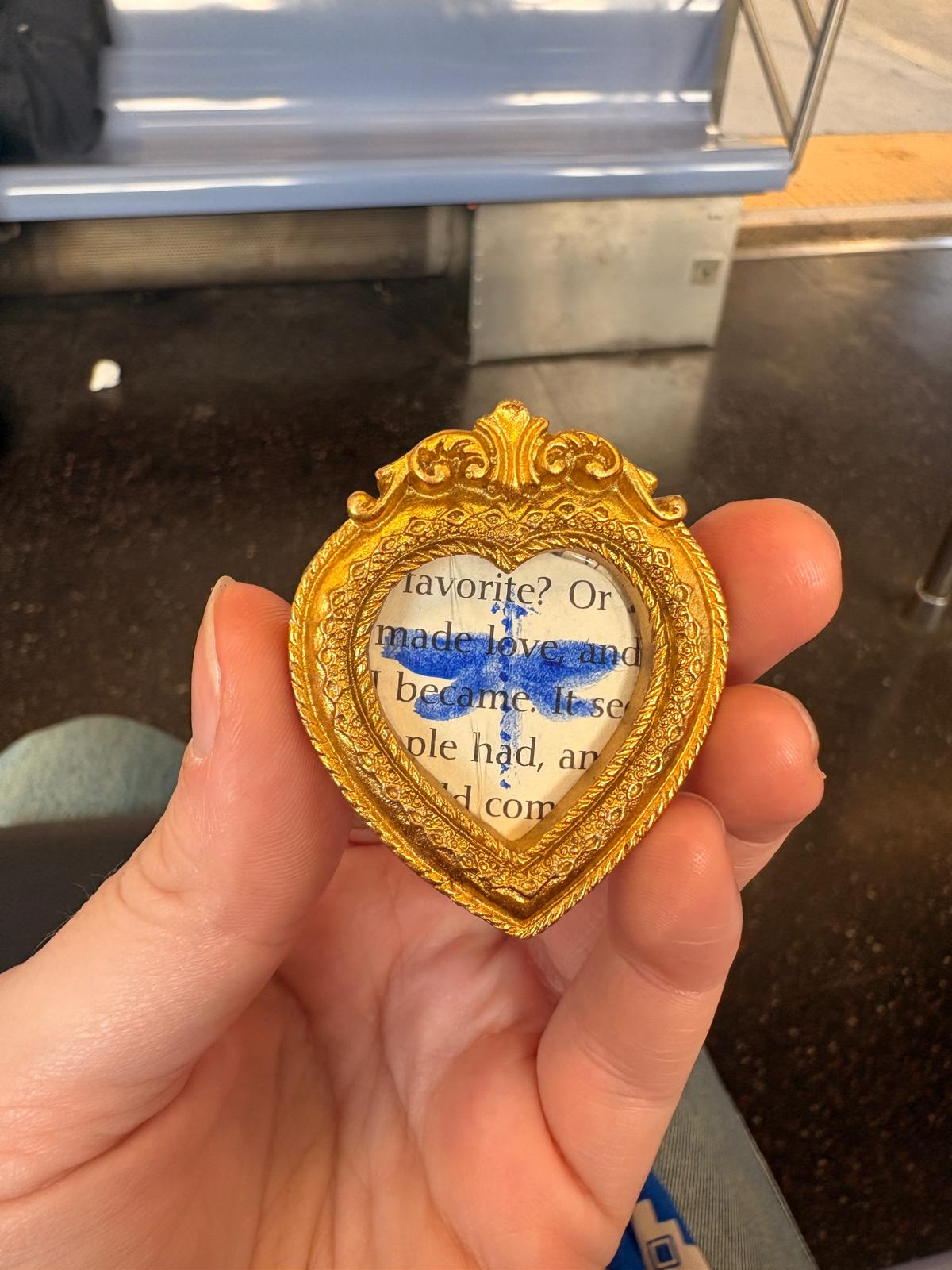 Blue dragonfly on a book page in a gold heart frame